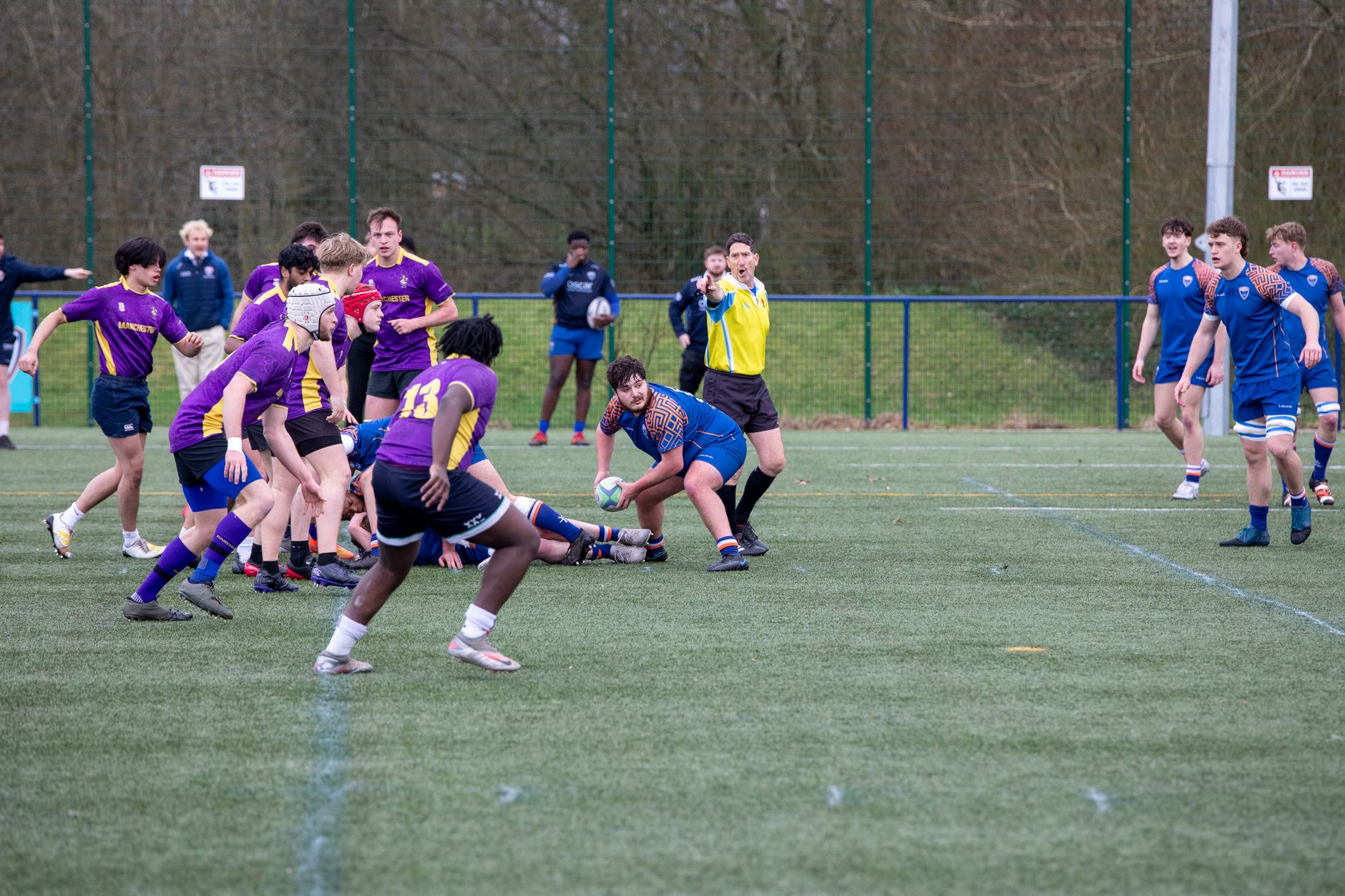 Joueurs de rugby disputant une action sur un terrain sous le contrôle de l’arbitre.