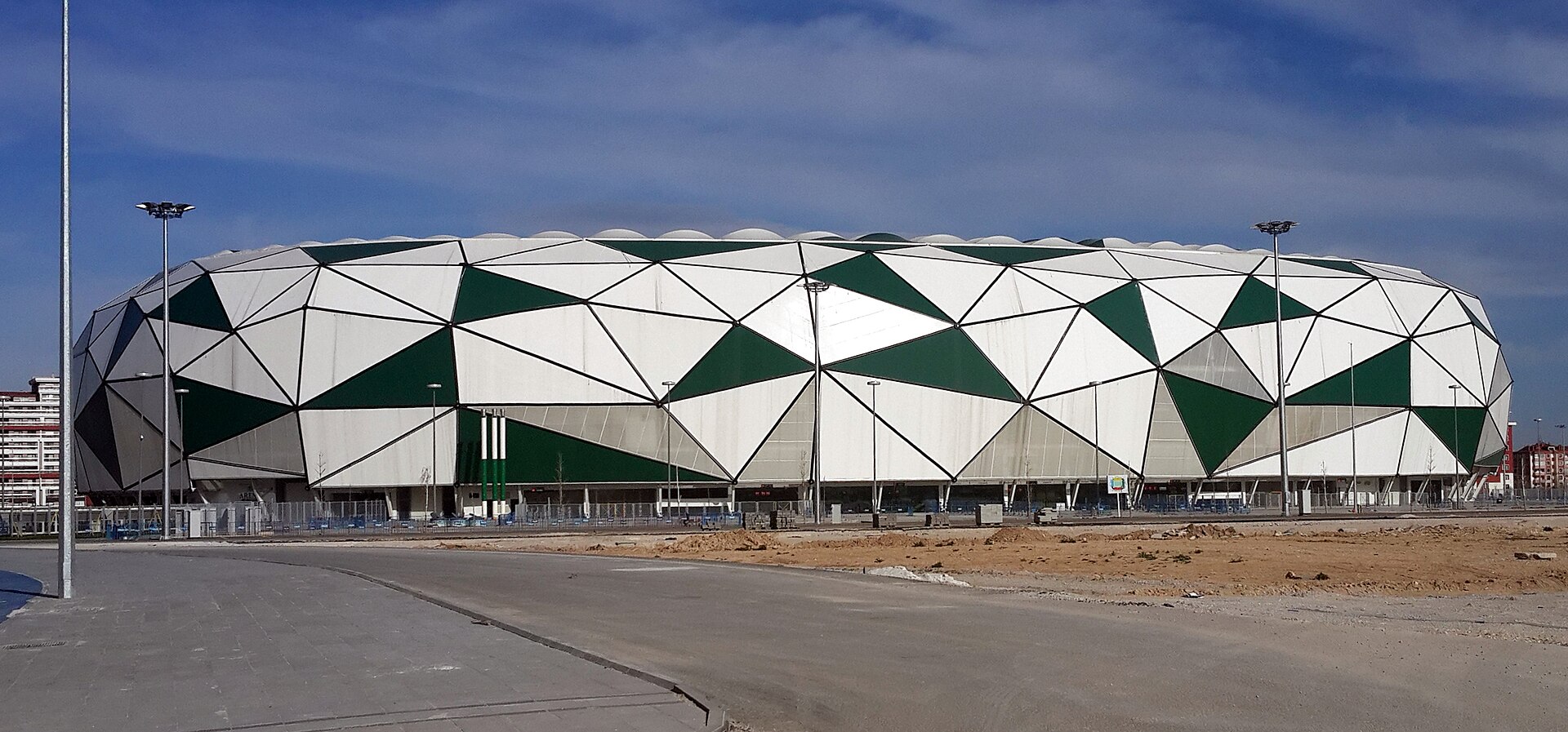 La façade en triangles blancs et verts d'un stade de football, vue depuis un parking vide