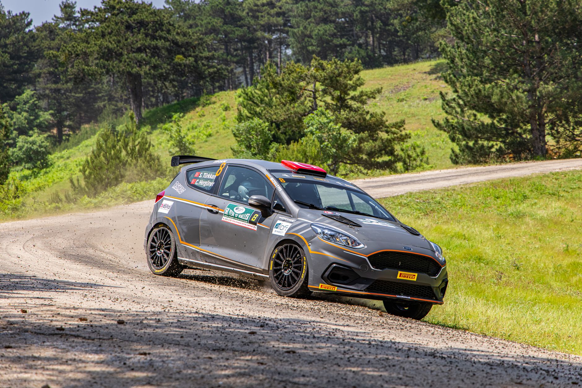 Voiture de rallye grise roulant à vive allure sur un chemin de terre et de gravier.